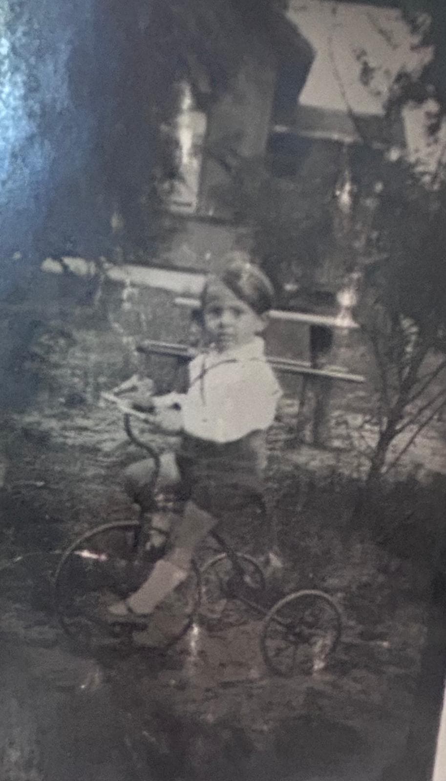 Very dark, blurred black-and-white snapshot of a small boy on a tricycle