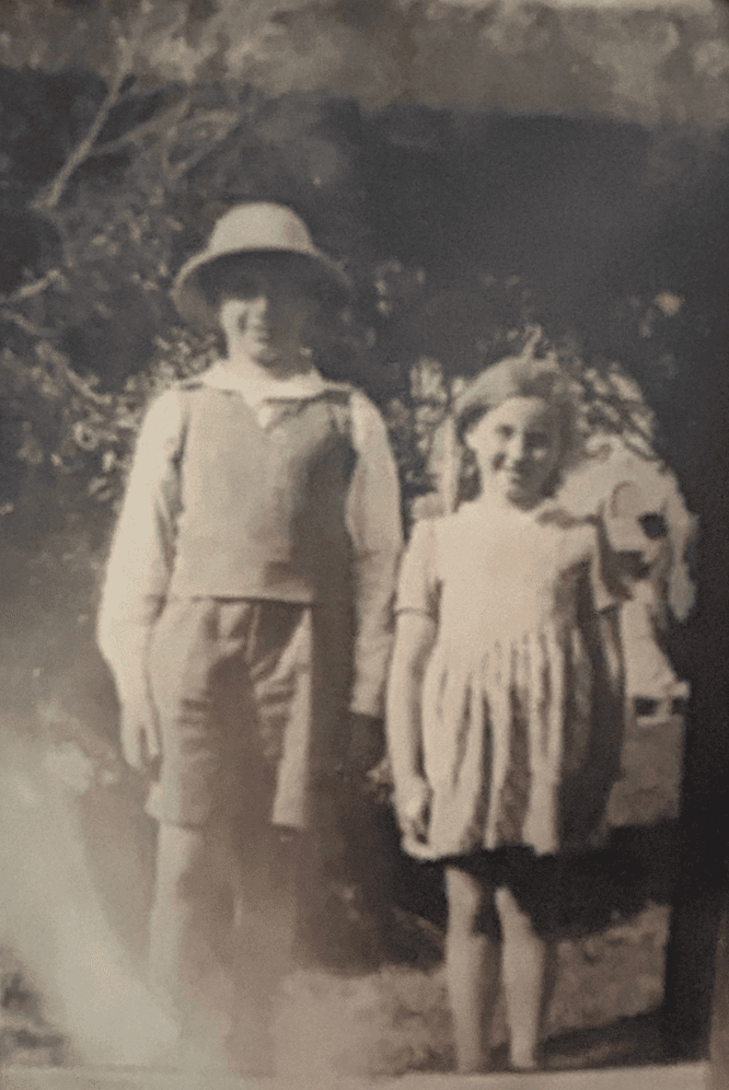 Faded sepia photo of a boy in a sun hat beside his younger sister