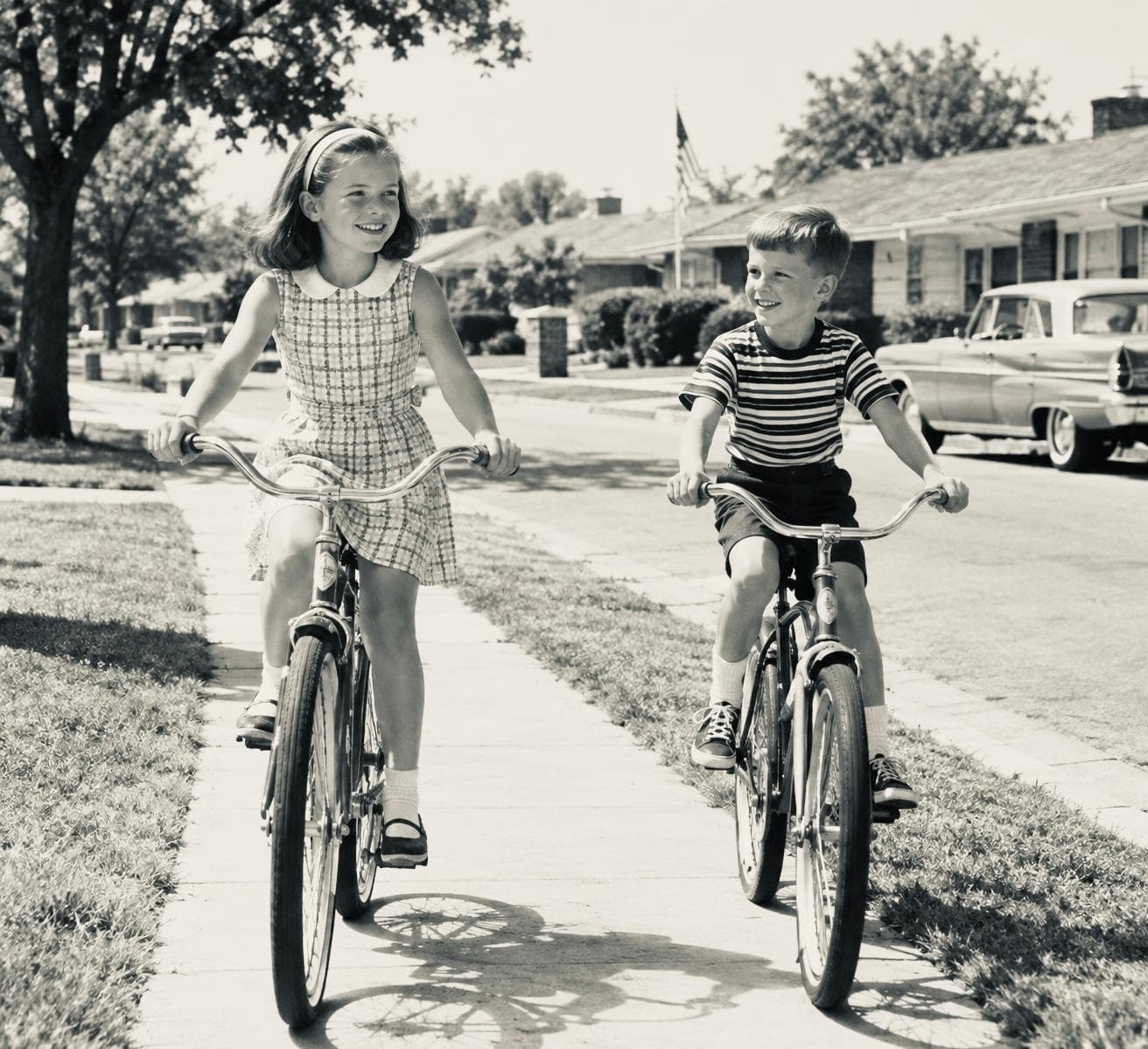 Black-and-white 1960s photo of a girl and a boy riding bicycles